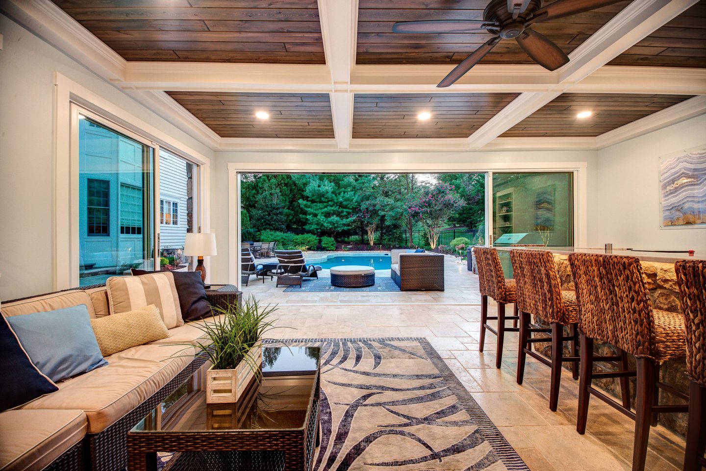 Covered outdoor living room and kitchen opening onto a pool terrace