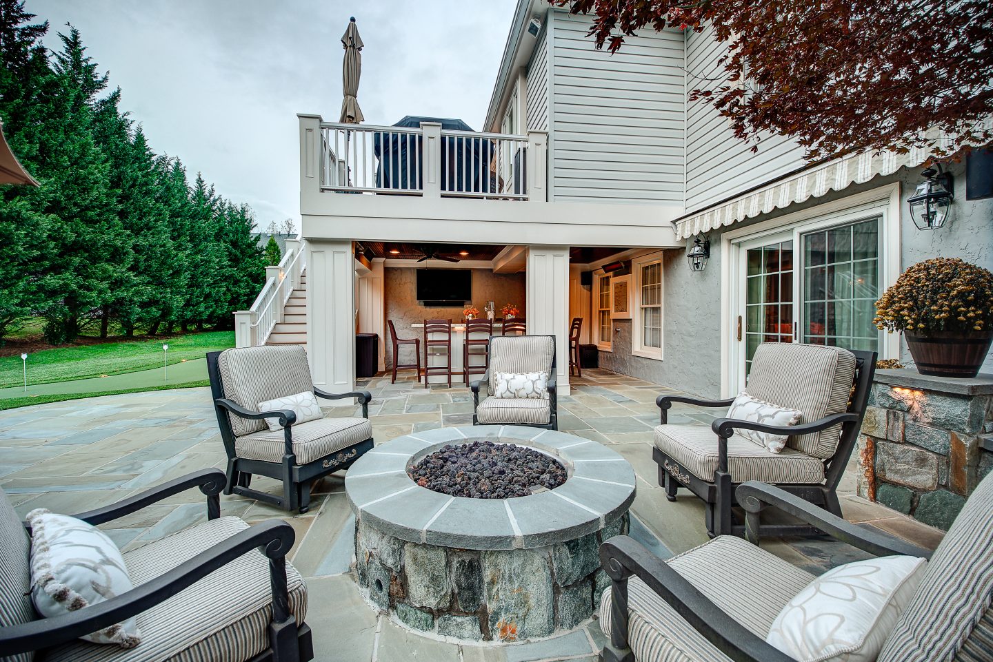 Outdoor lounge with upholstered seating and a fire feature beside a covered entertaining space