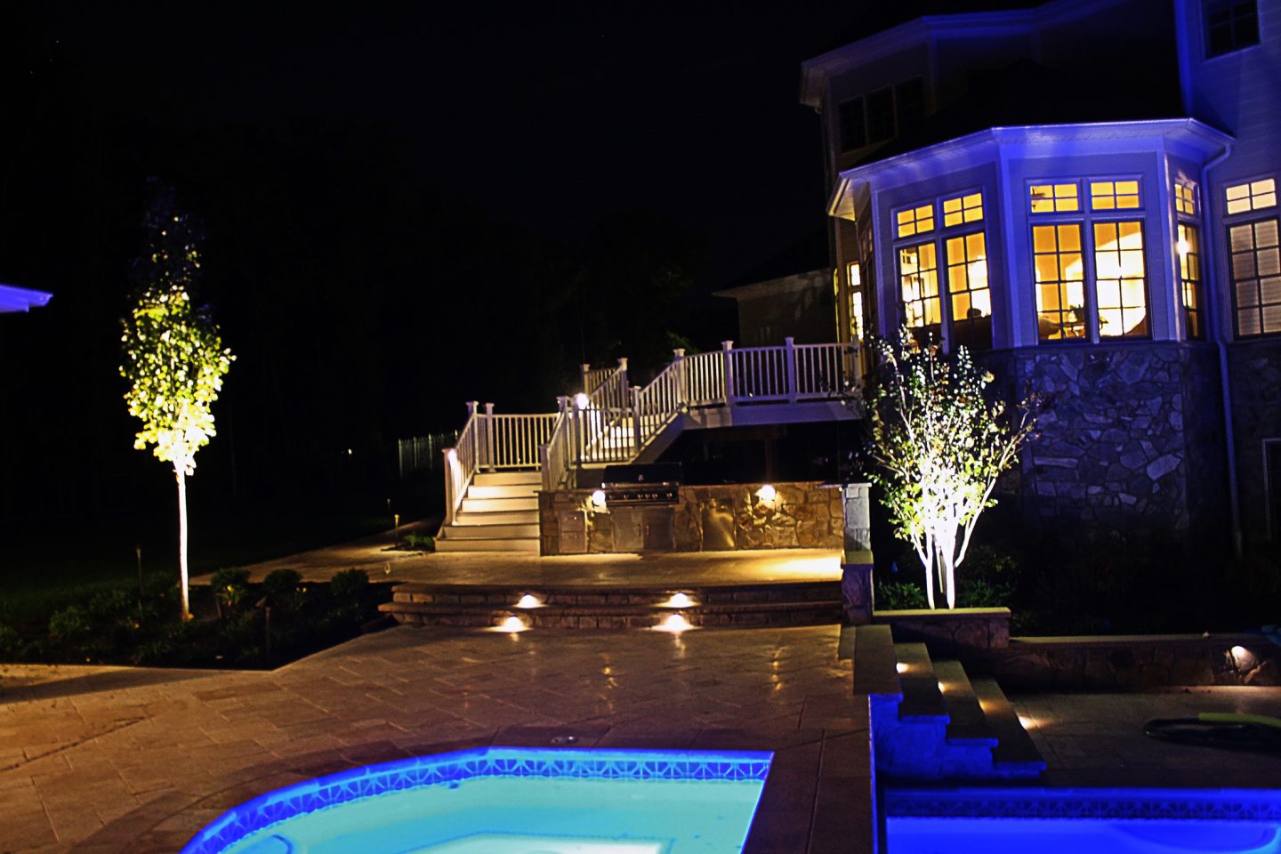 Landscape lighting on steps, trees and a lit spa at night