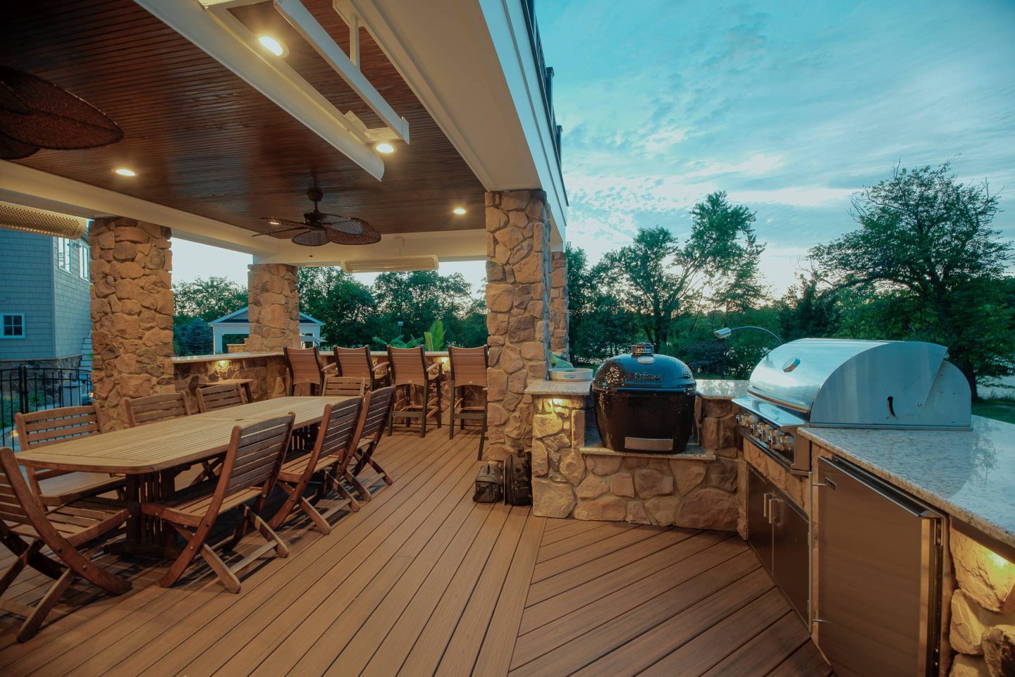 Covered outdoor kitchen and dining deck opening onto a green backyard