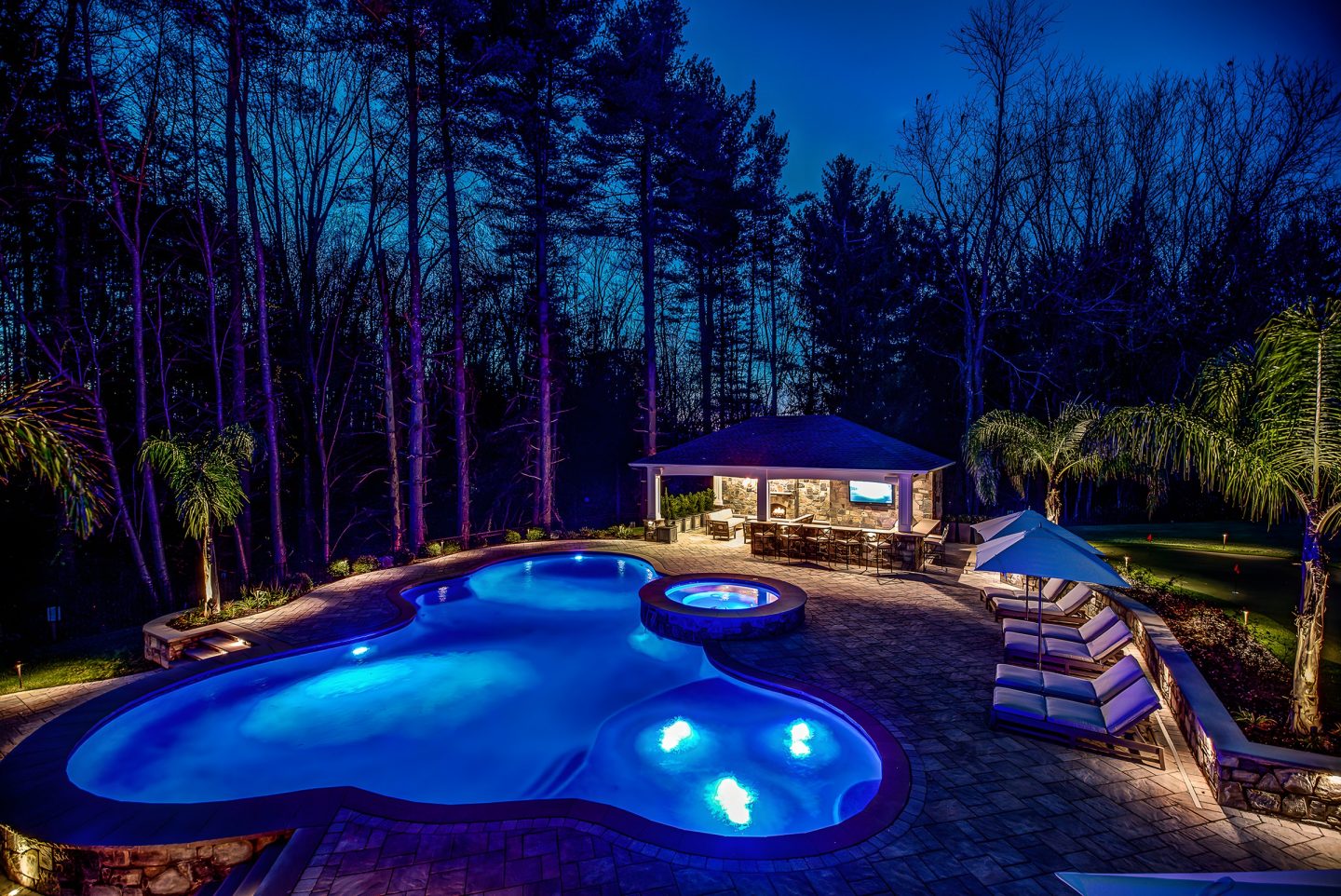 Pool with underwater lighting at night in a backyard with pavilion