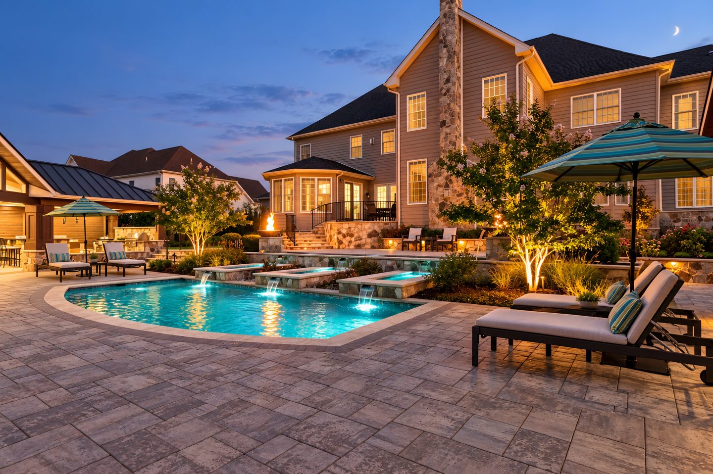 Landscape architecture in a residential setting with stone patio and illuminated pool at dusk