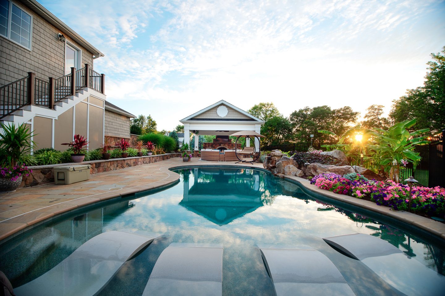 Custom pool reflecting the evening sky, with a stone terrace and garden pavilion