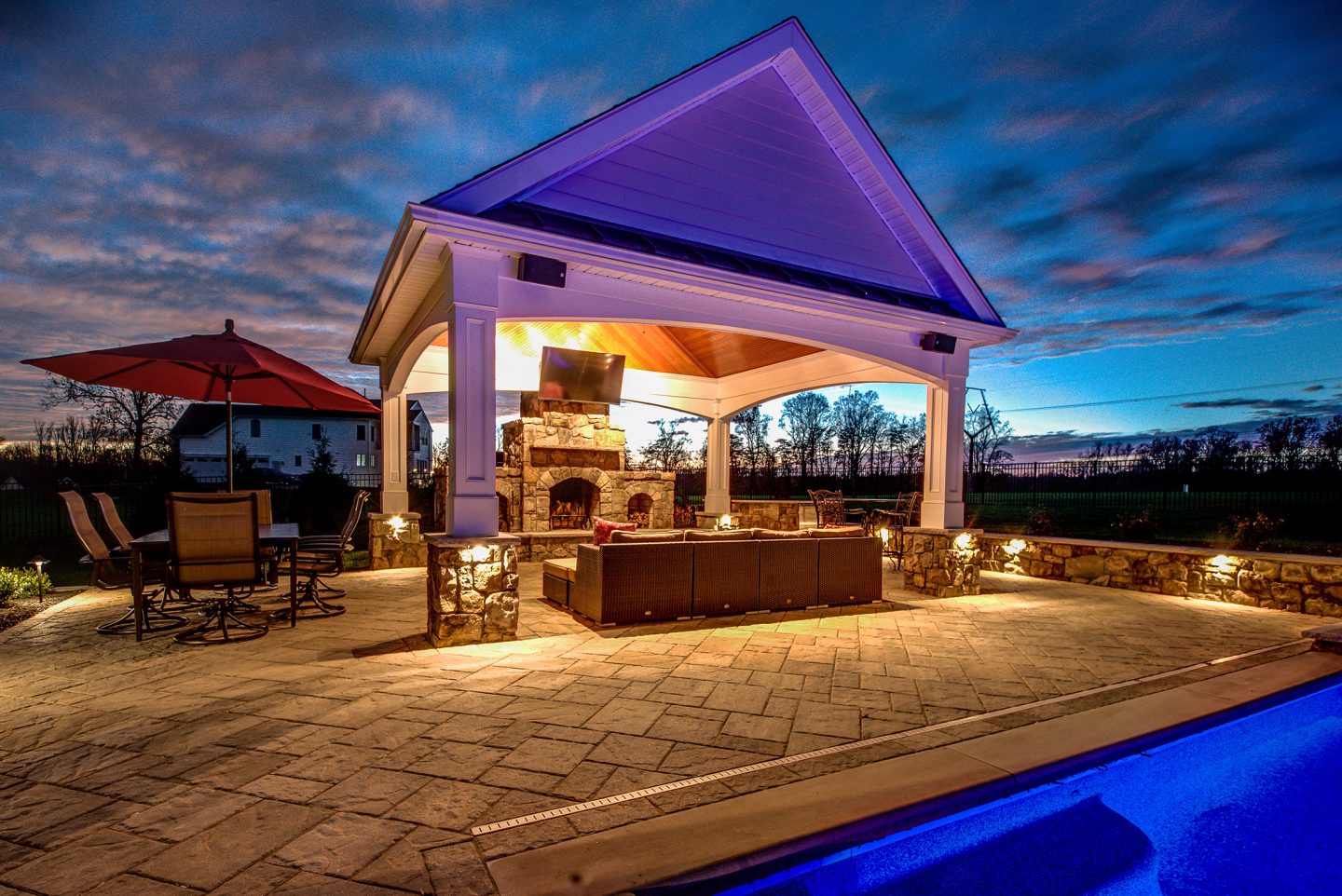 Pavilion with outdoor kitchen and lighting at dusk beside a pool