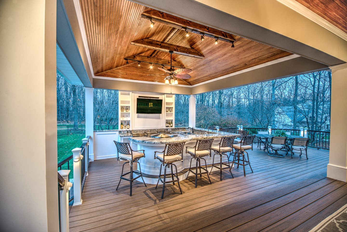 Covered outdoor kitchen and dining area with warm ceiling lights and a woodland outlook