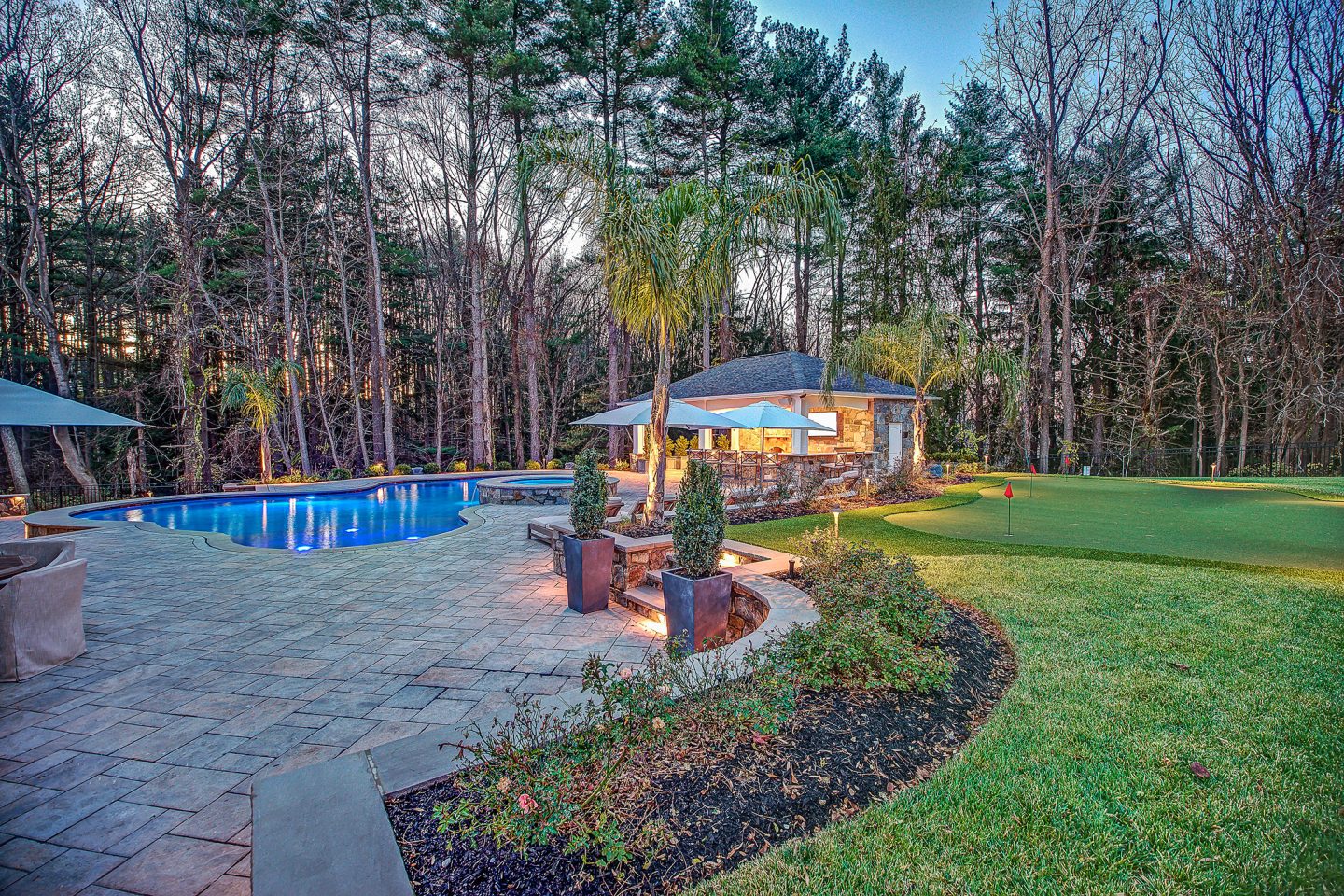 Stone pool terrace with planted borders and a timber pavilion in the distance