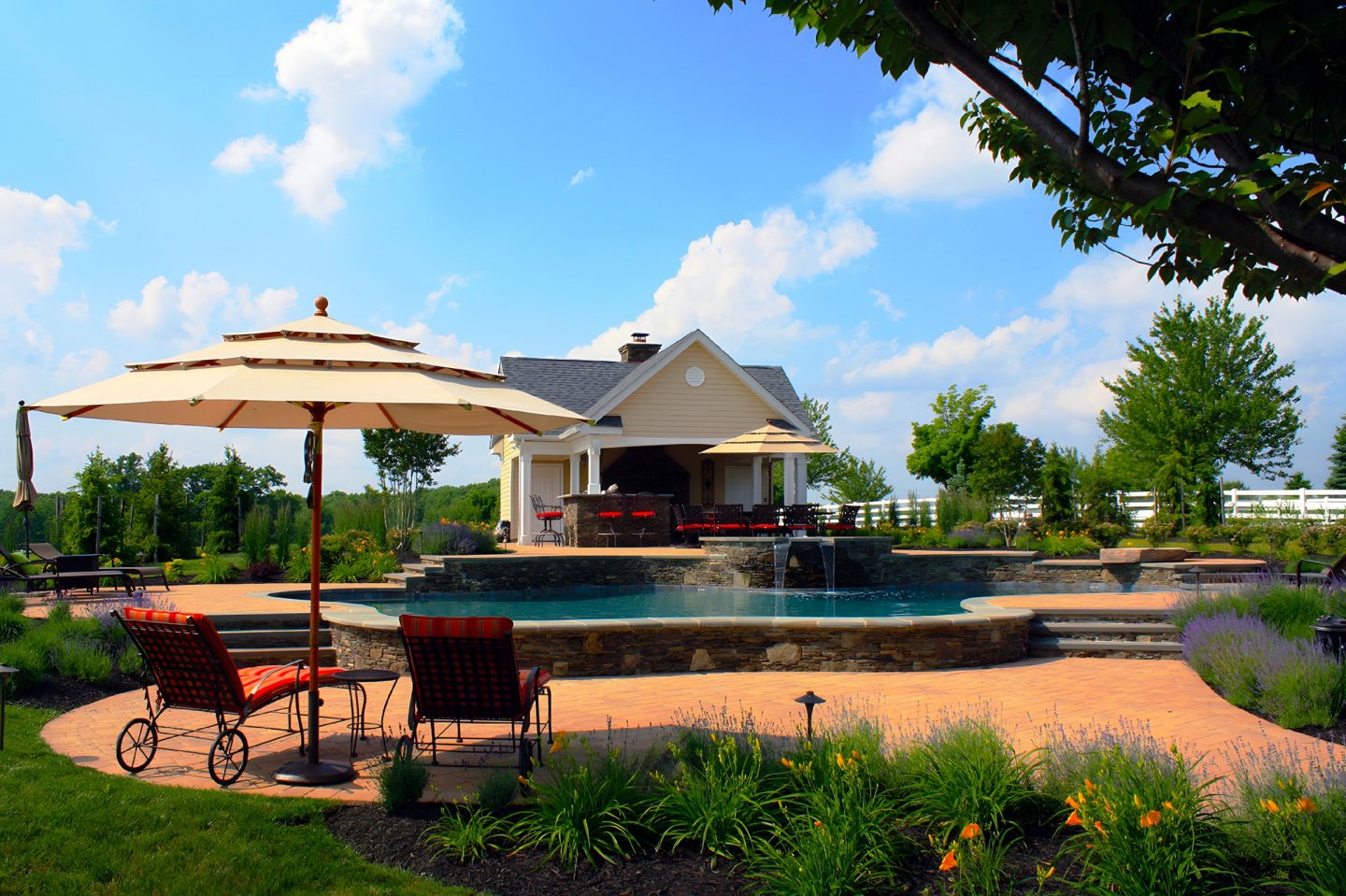 A backyard featuring a pool with a waterfall and a stone patio under a clear sky