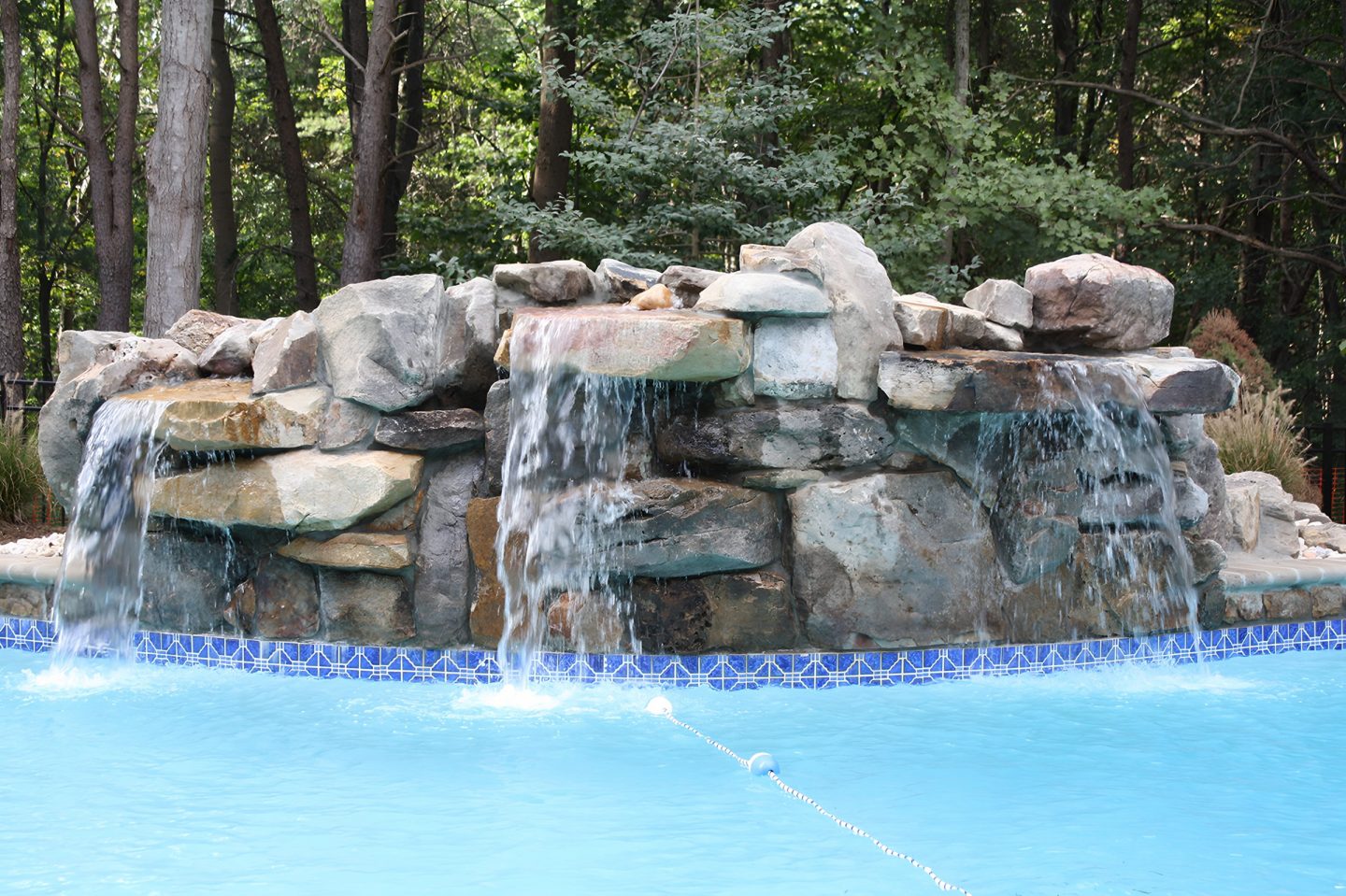 Rock waterfall with multiple streams flowing into a pool surrounded by trees