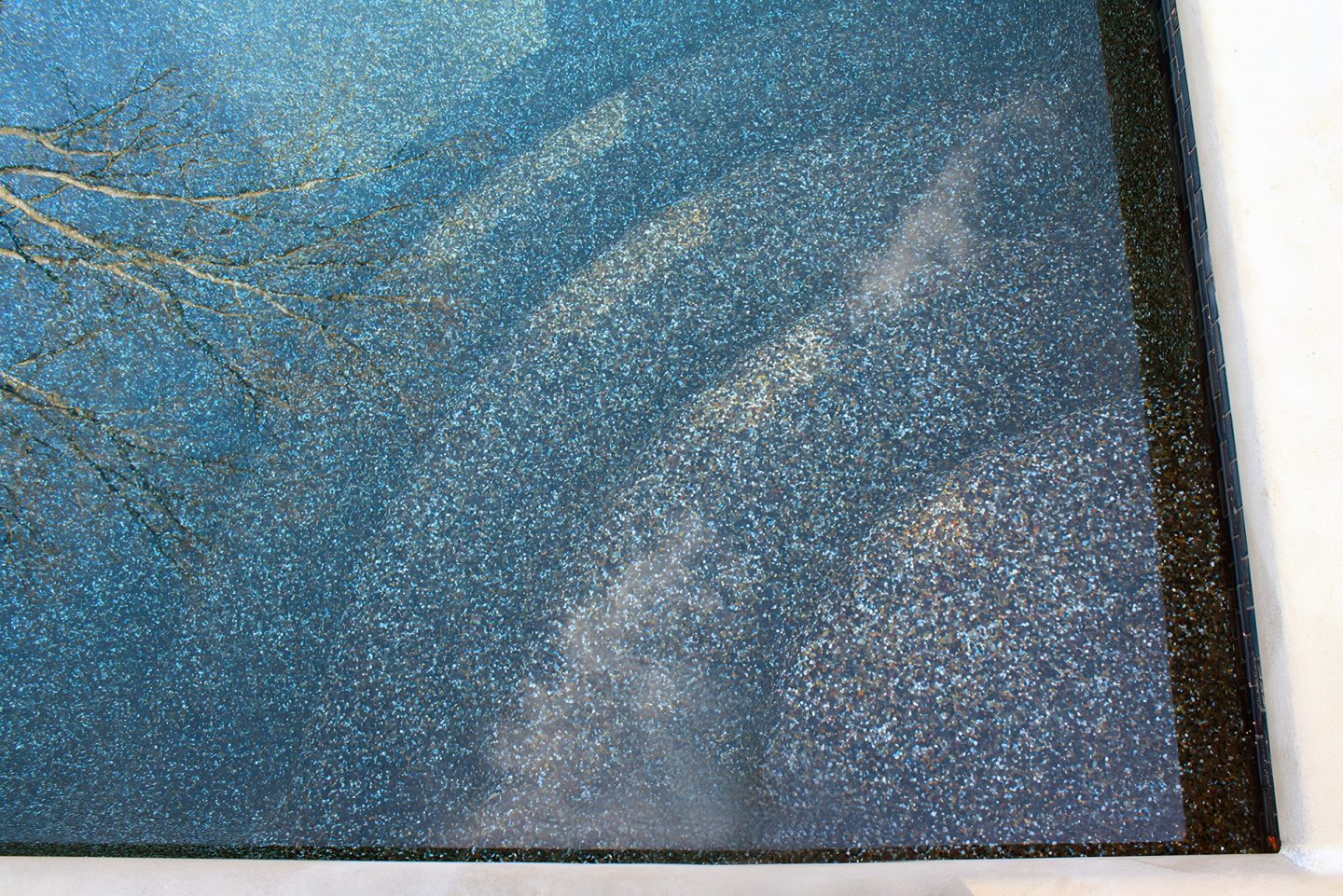 Blue aggregate pool surface with branch reflections
