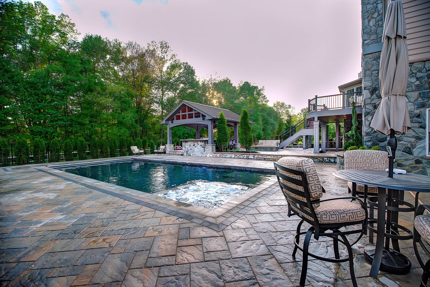 Pool in a residential backyard with a waterfall and stone patio