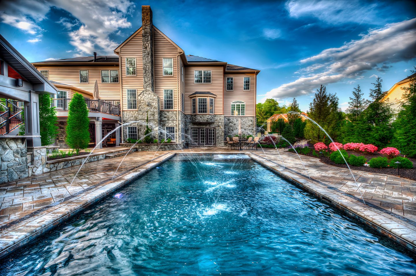 Rectangular pool with fountains surrounded by stone patio and mature landscaping