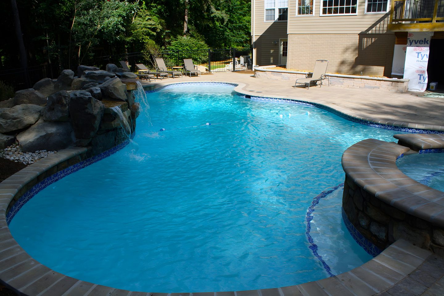 Residential swimming pool in backyard with stone waterfall