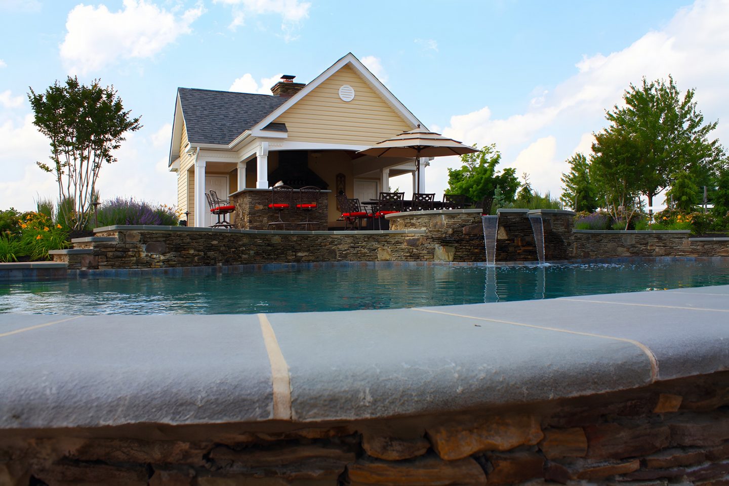 Pool area with stone wall and waterfalls in a suburban backyard