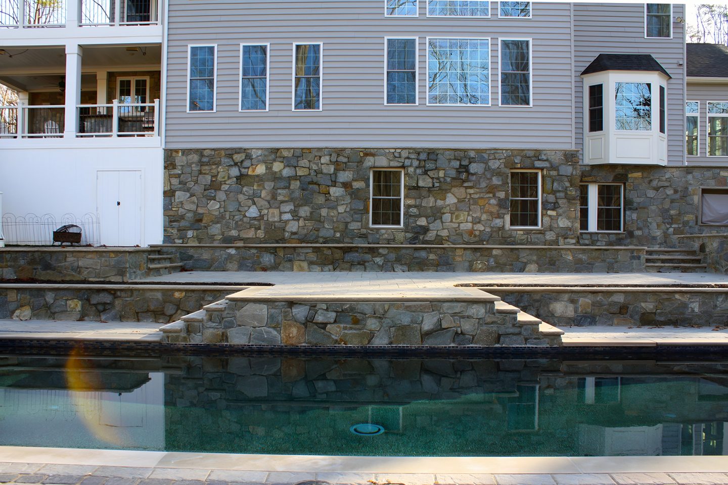 A swimming pool and multi-level terrace with stone retaining walls in a residential backyard