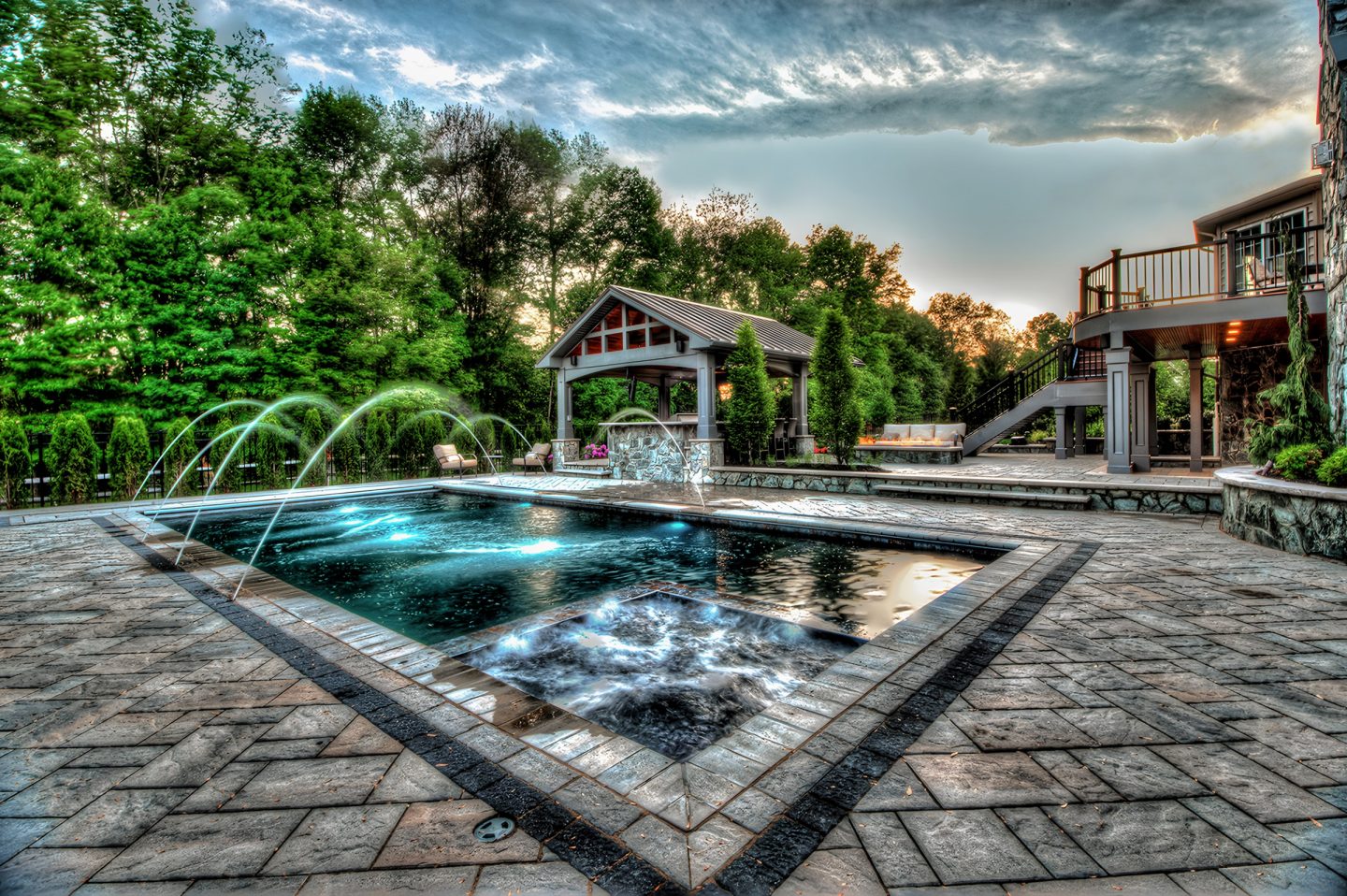 A pool and spa with water jets in a residential backyard at dusk