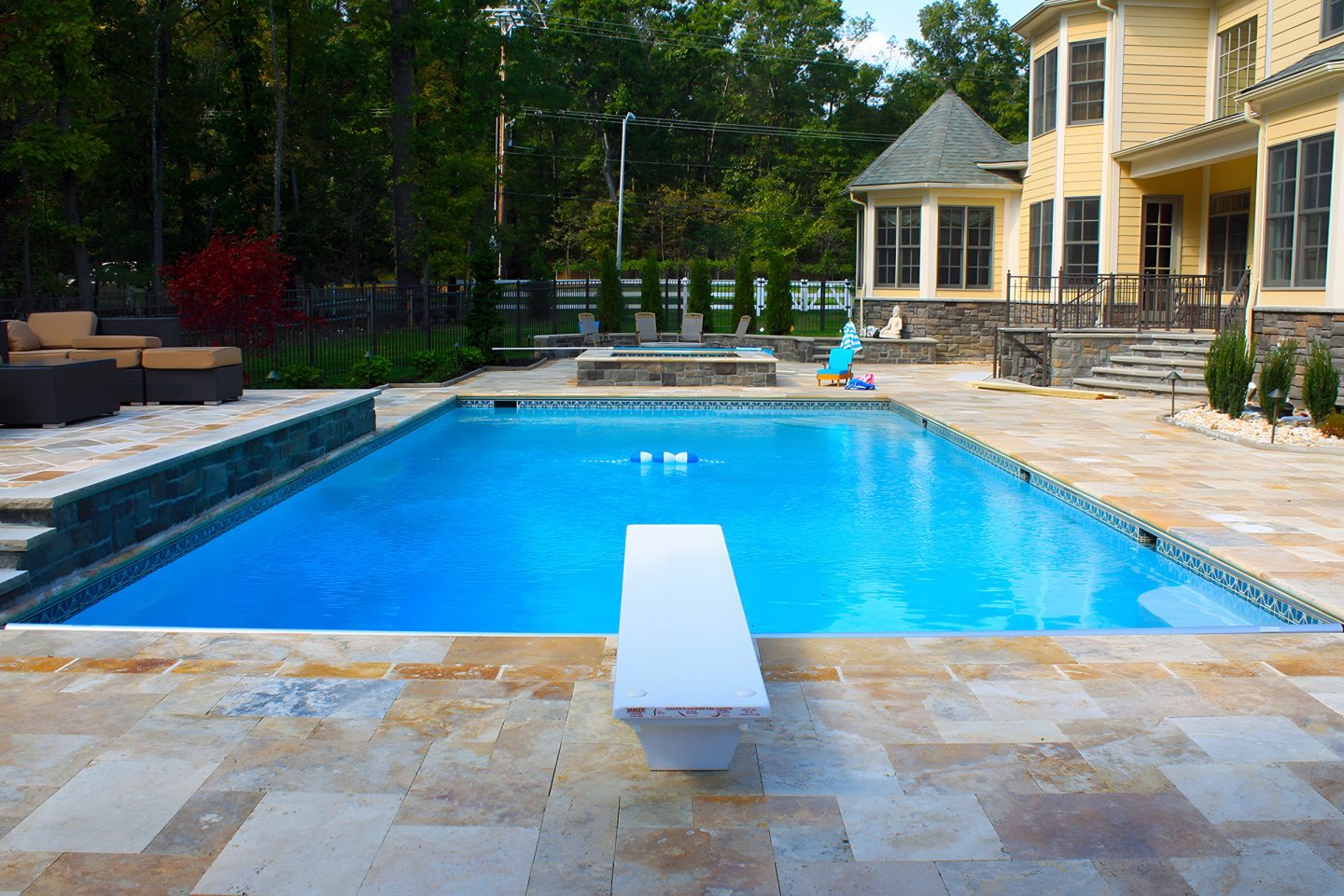 A swimming pool with a diving board in a backyard patio area