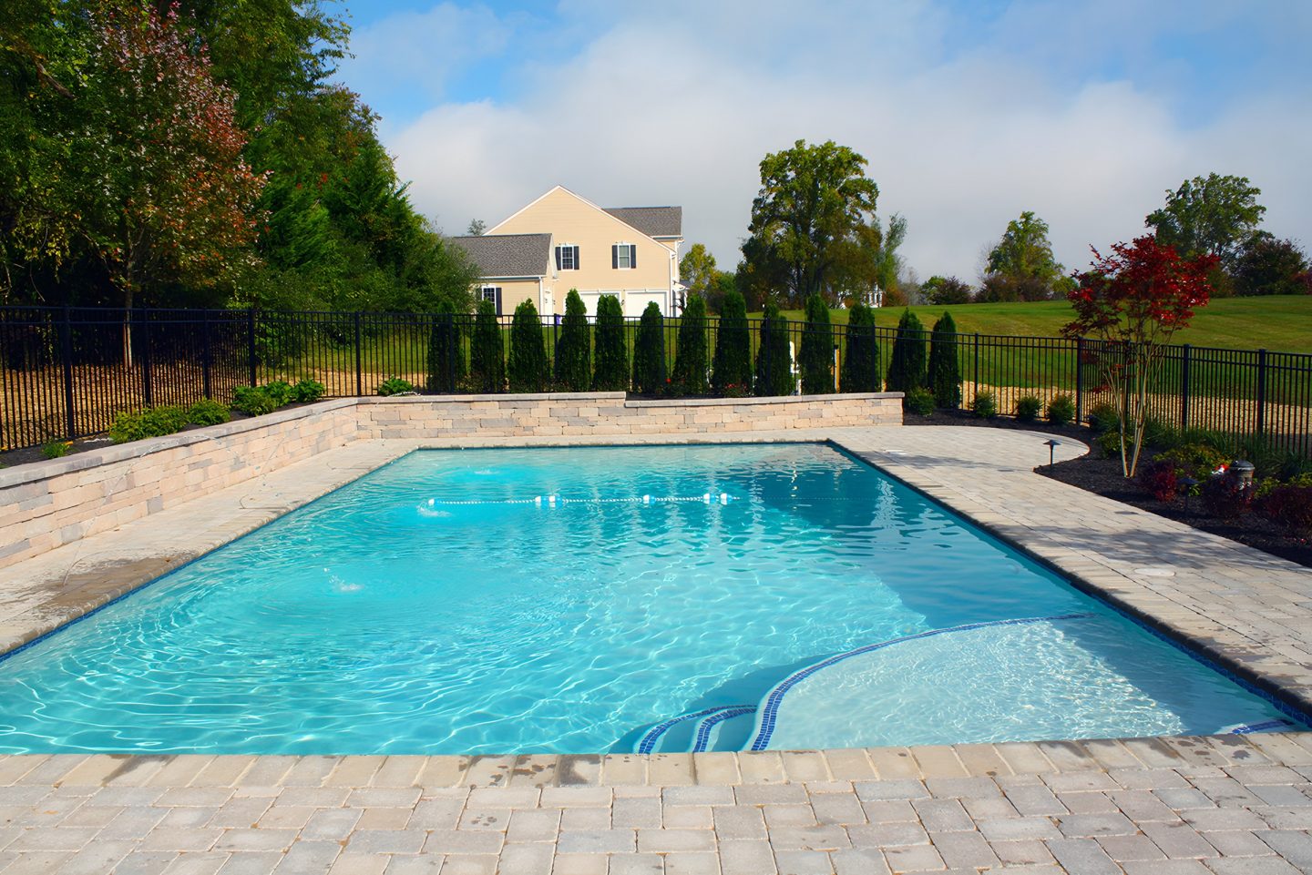 A pool with a paver deck and stone retaining wall in a residential backyard