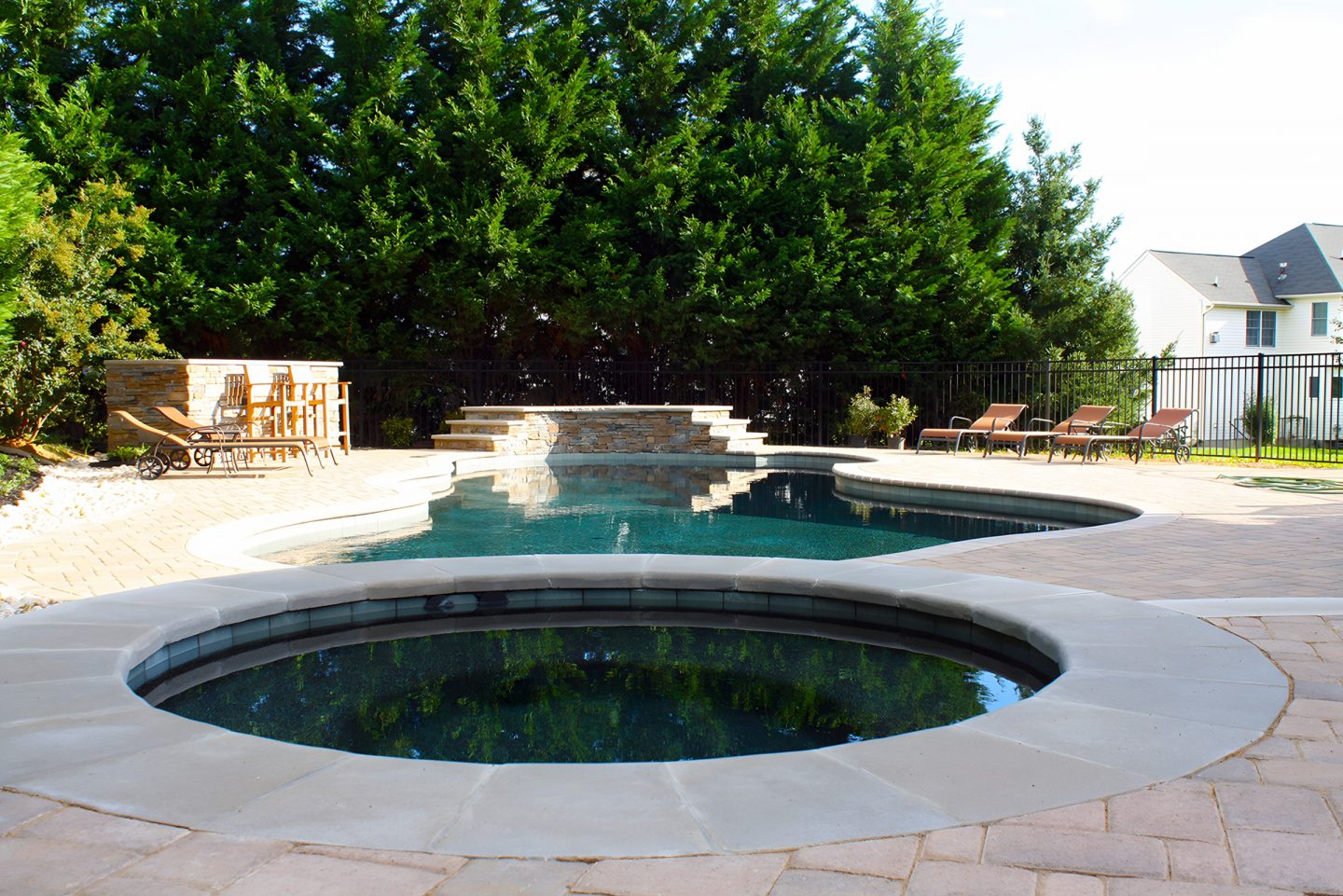 Pool in backyard with stone coping and outdoor kitchen