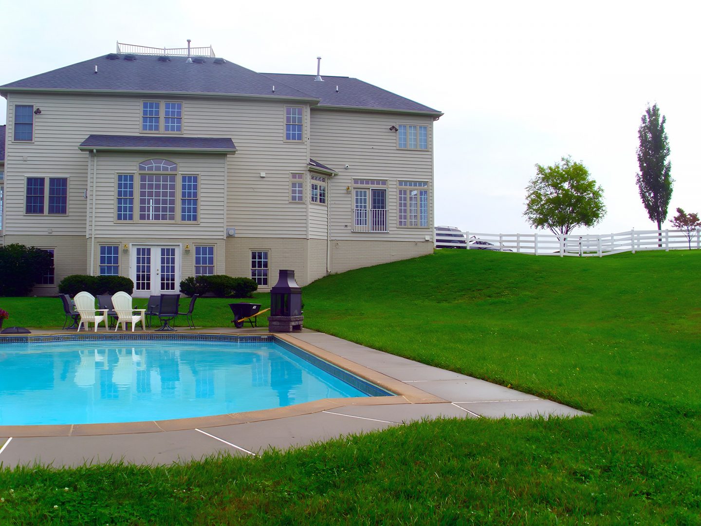 A swimming pool in a residential backyard with lounge chairs on a concrete deck
