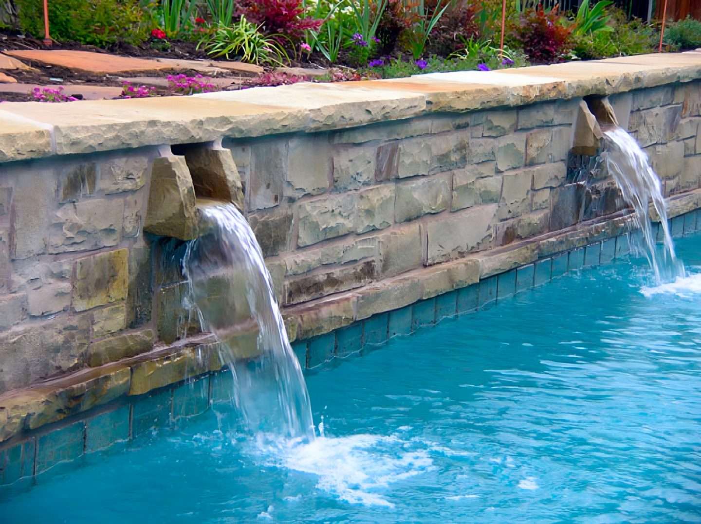 Waterfalls flow from a stone retaining wall into a swimming pool.