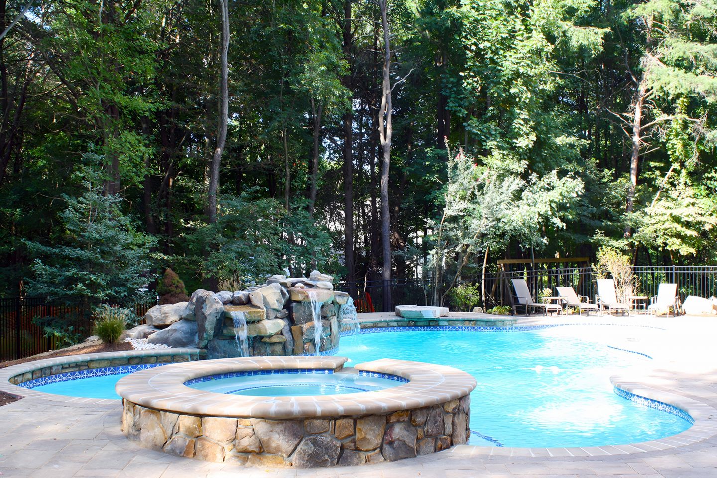 Pool and spa with rock waterfall in tree-lined backyard