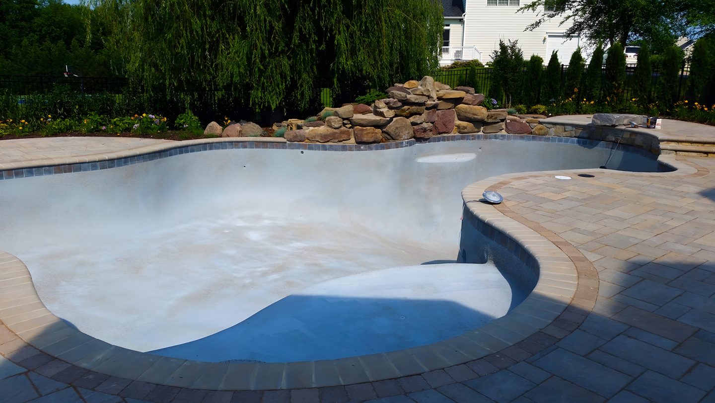 Empty swimming pool in residential backyard with rock stack