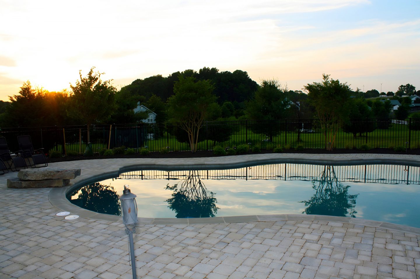 A swimming pool enclosed by a black metal fence with trees planted along the yard perimeter