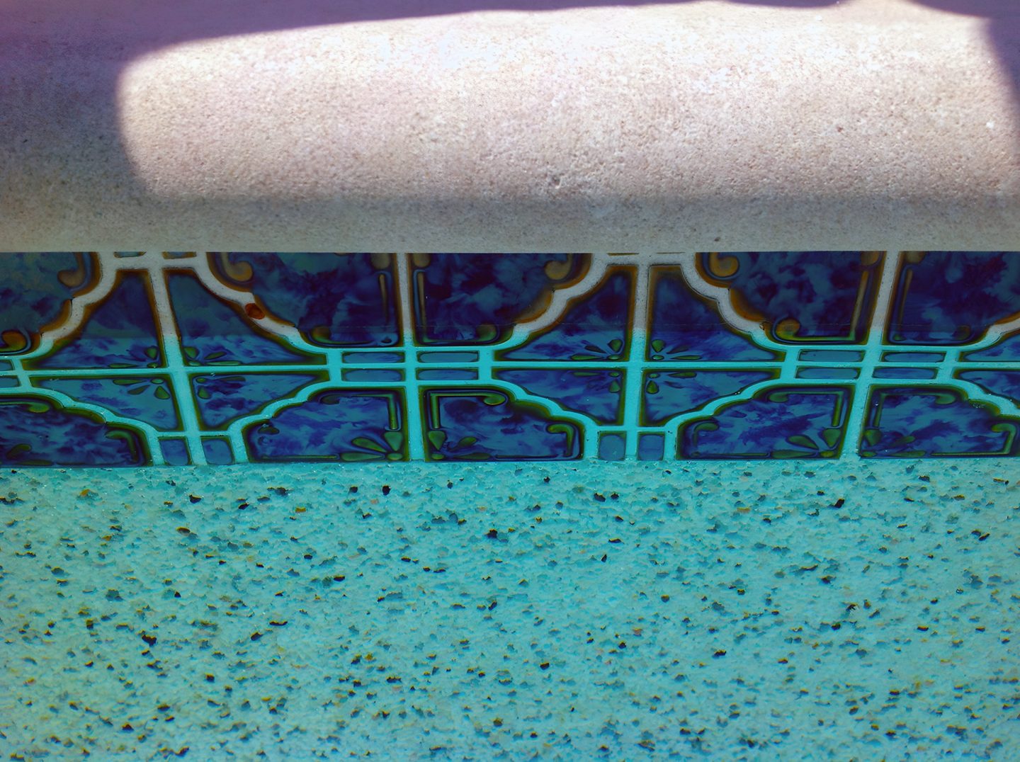 A pool edge with decorative tiles and a textured concrete surface.