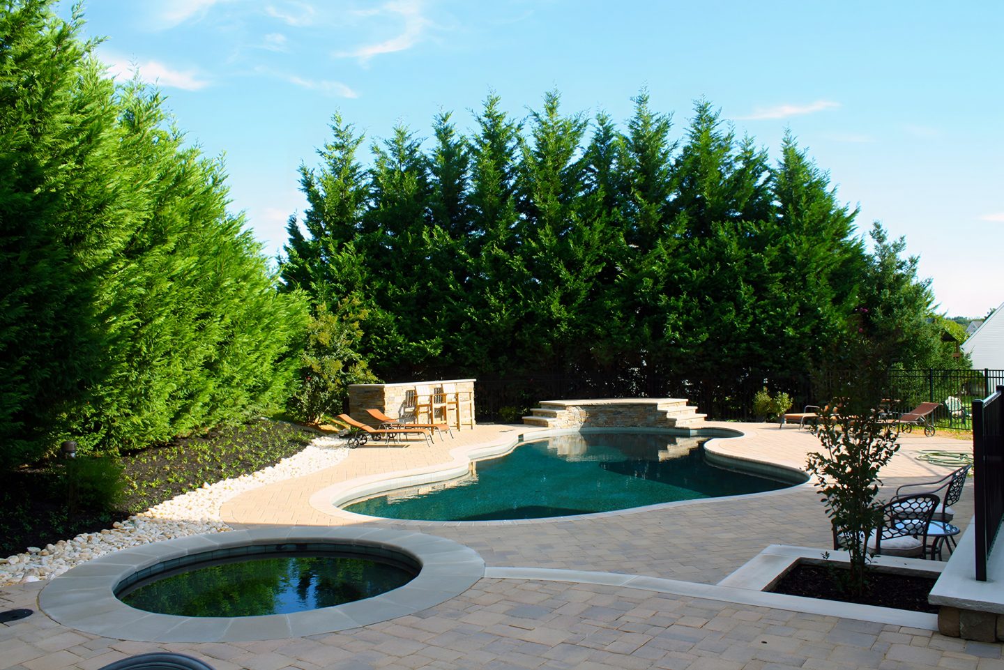 Pool and hot tub in a residential backyard with privacy trees