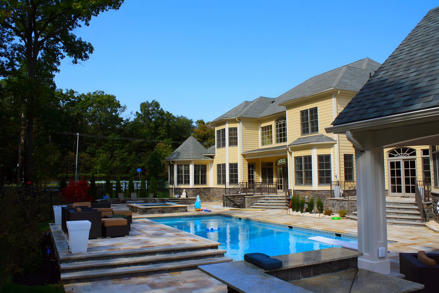 A swimming pool and stone patio next to a yellow house