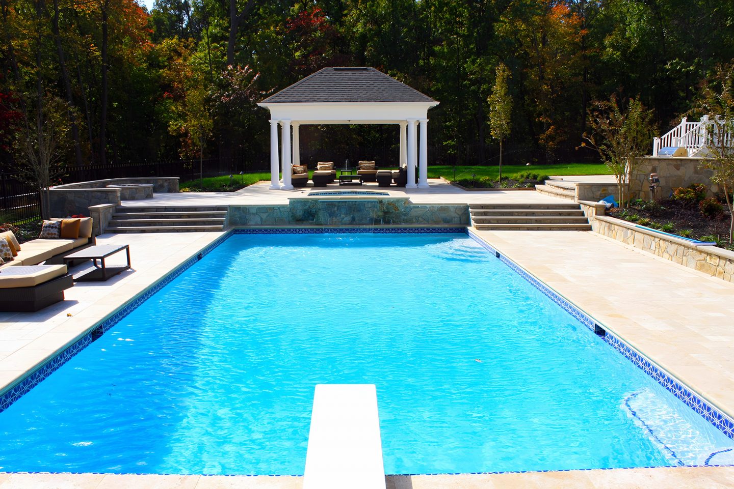 A swimming pool in a backyard with a gazebo at the far end
