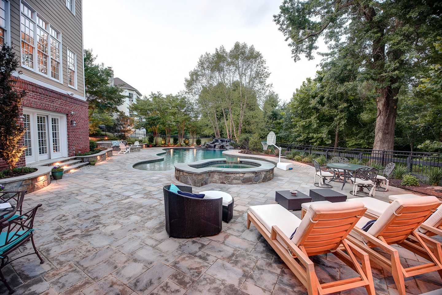 A kidney-shaped swimming pool and spa sit on a flagstone patio in a residential backyard.