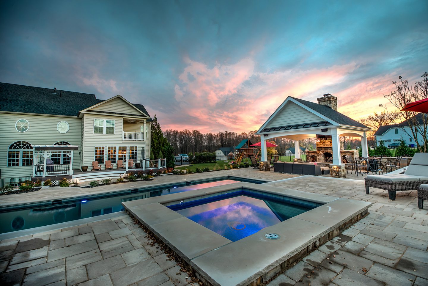A swimming pool and spa in a backyard at dusk