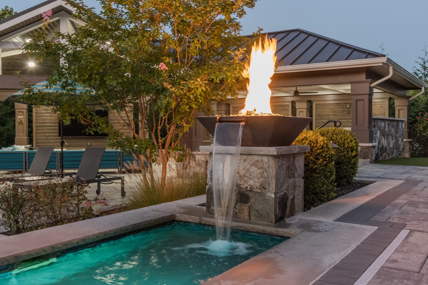 A stone pedestal holds a burning fire bowl above a waterfall flowing into a blue pool.