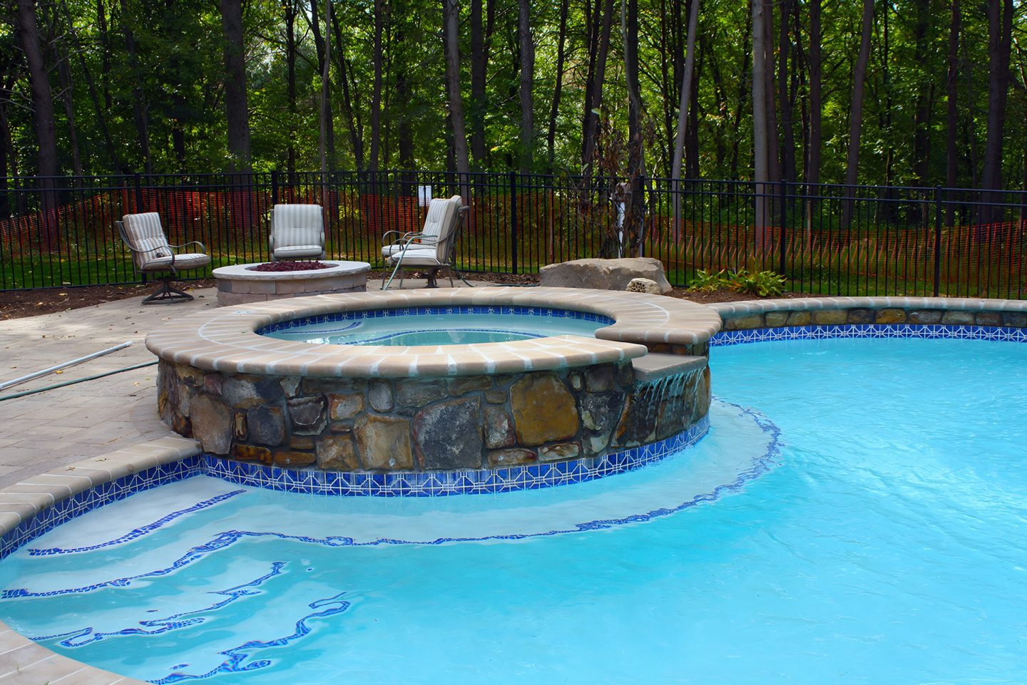 A -built hot tub with a stacked stone base sits on a patio next to a swimming pool.
