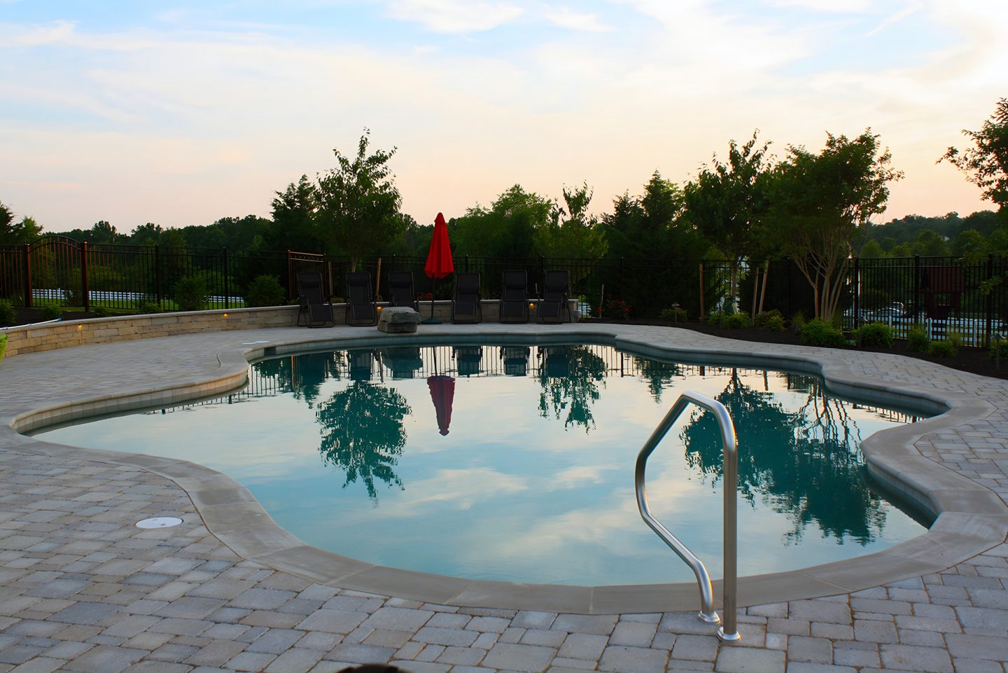 A serene backyard pool at dusk with trees and a clear sky
