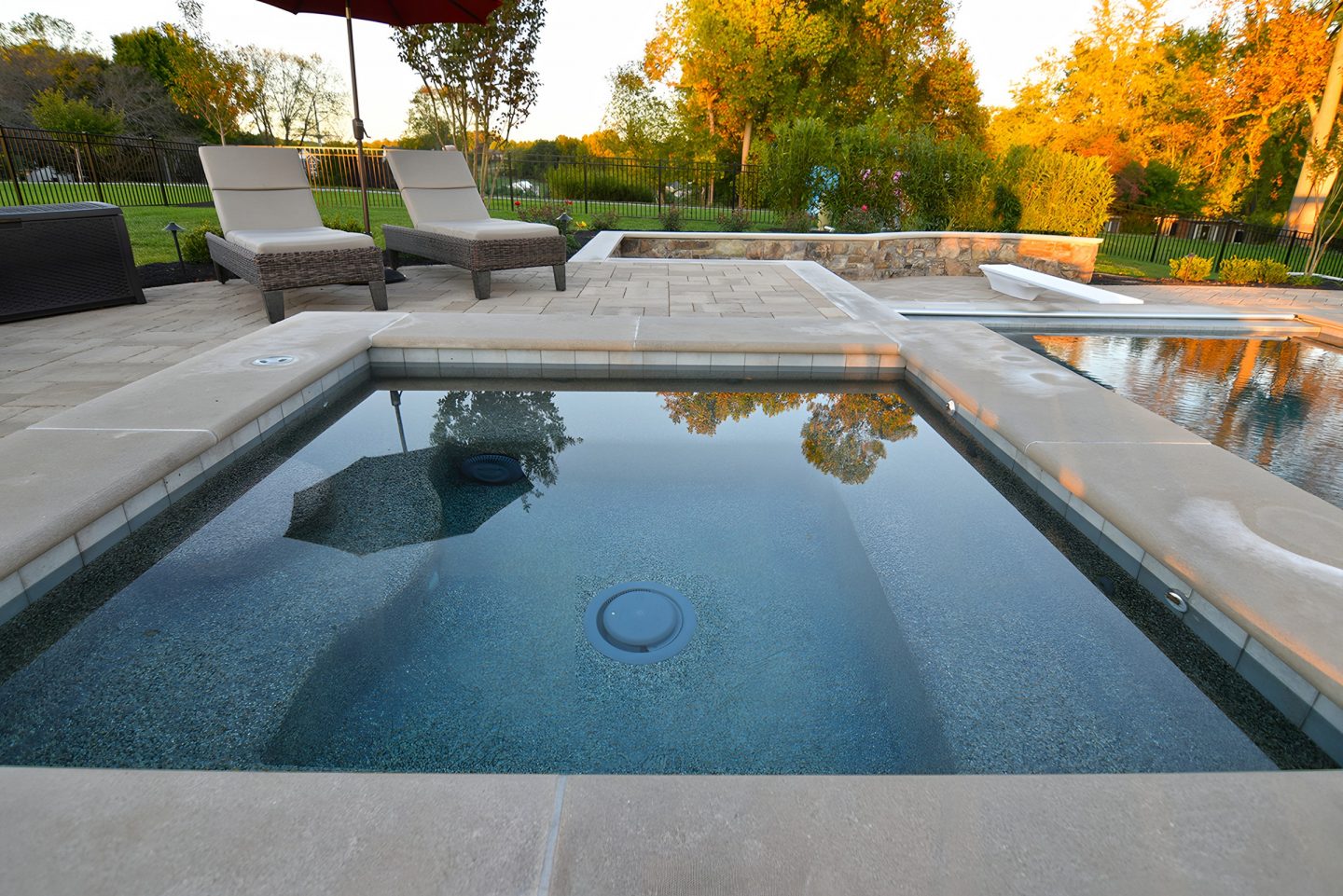 A stone coping pool and spa structure sits on a paved backyard patio with integrated water features.