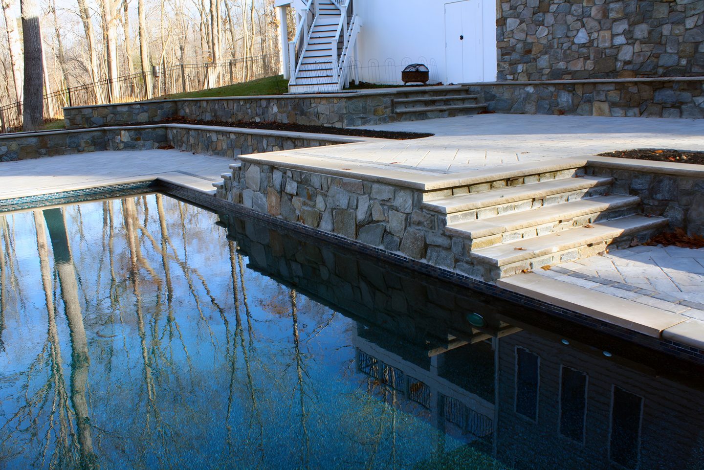 A swimming pool with stone retaining walls and concrete steps in a residential backyard