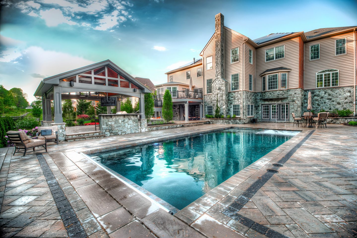 Pool in a residential backyard with stone patio and covered pergola