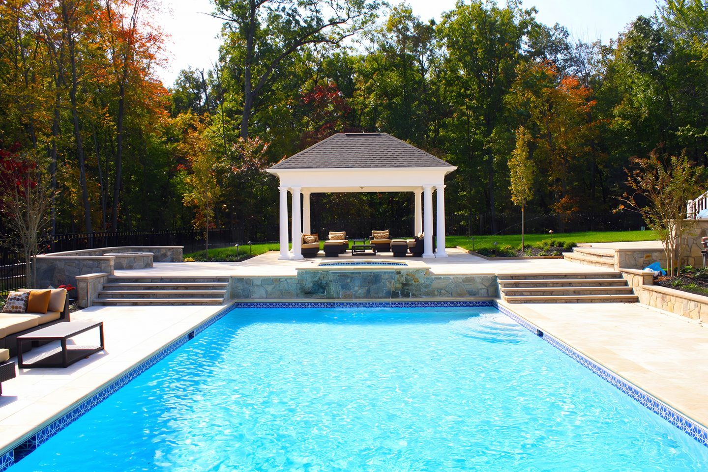 A pool and spa in a residential backyard with stone steps and retaining walls.