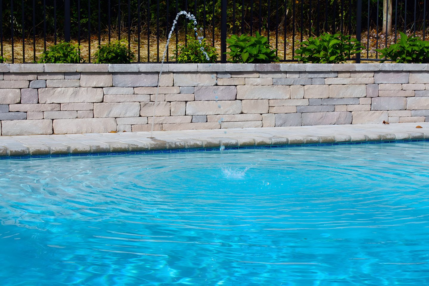 A swimming pool with a water fountain feature and stacked stone retaining wall.