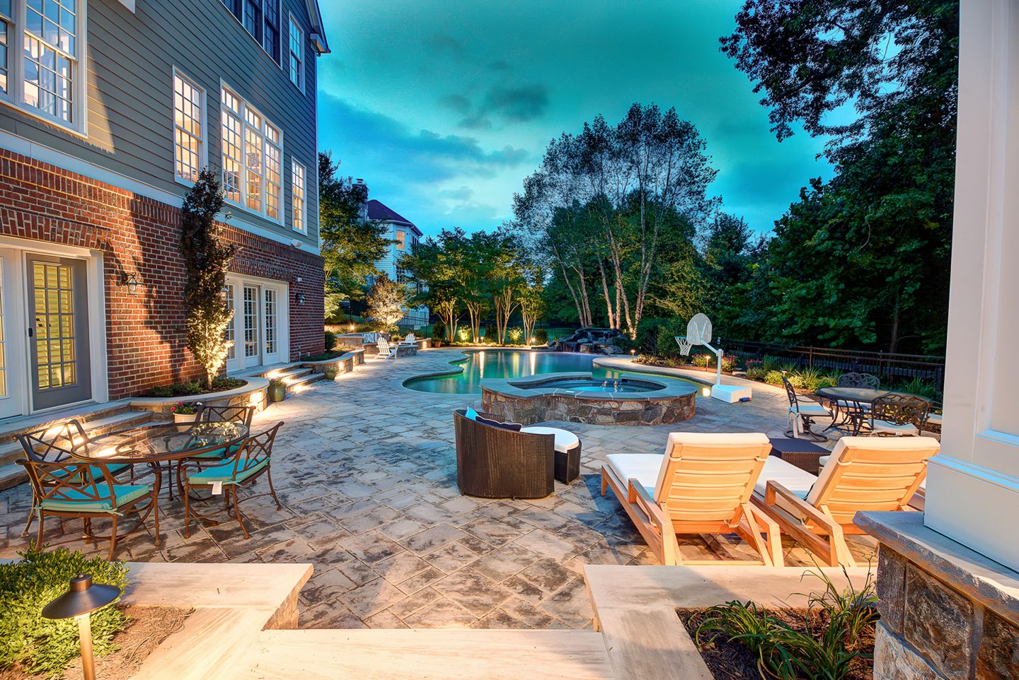 Inground swimming pool in a residential backyard with stone patio and evening lighting